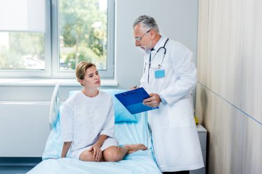 olgun erkek doktor stetoskop Pano bayan hasta hastane odasında işaret eden boyun üzerinden ile 