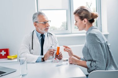 Orta yaşlı erkek doktor Bayan hasta masada office haplara işaret 