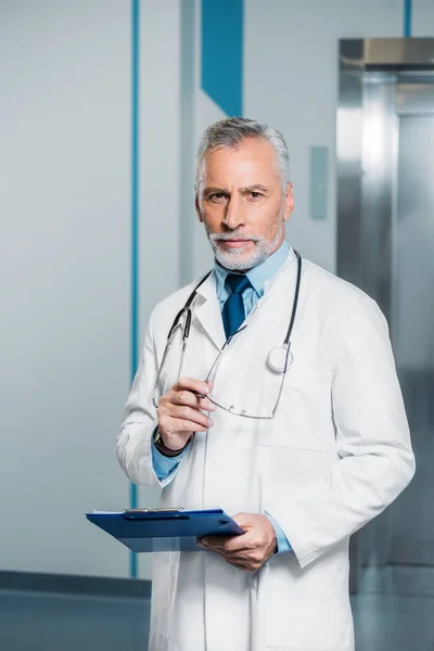 Middle Aged Male Doctor Stethoscope Neck Holding Eyeglasses Clipboard Looking — Stock Photo, Image