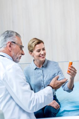 Bayan hasta hastane odasında hap vererek olgun erkek doktor gülümseyen