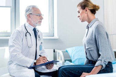 olgun erkek doktor Bayan hasta hastane odasında yakınındaki Pano yazma yan görünüm