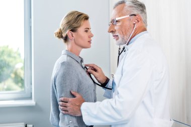 olgun erkek doktor muayene kadın hasta hastane odasında stetoskop tarafından yan görünüm