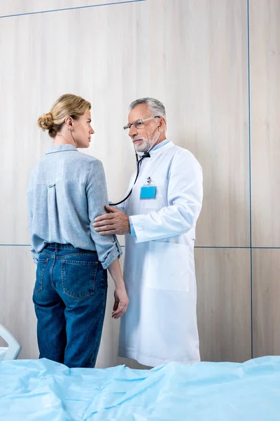 Confident Mature Male Doctor Examining Female Patient Stethoscope Hospital Room — Stock Photo, Image