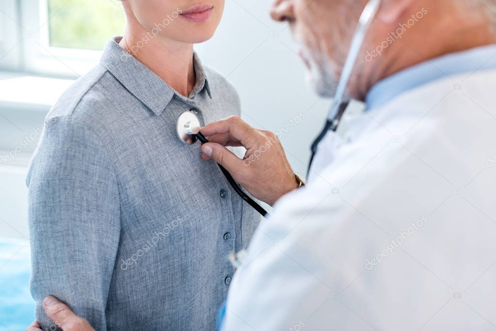 partial view of mature male doctor examining female patient by stethoscope in hospital room
