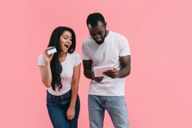mutlu genç Afro-Amerikan çift online dijital tablet üzerinde pembe arka plan izole kredi kartıyla alışveriş yaparken 