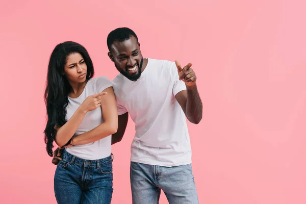 emotional african american couple pointing by fingers aside isolated on pink background
