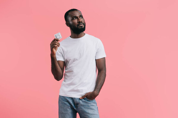 young african american man with condom looking away isolated on pink background 