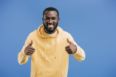 başparmak yukarıya üzerinde mavi arka plan izole hareketleri yapan mutlu genç Afro-Amerikan erkek