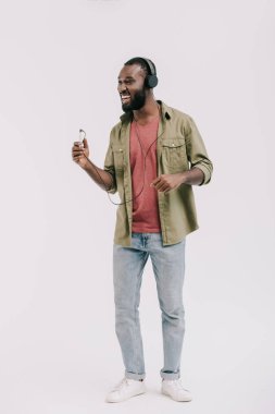 mutlu Afrika kökenli Amerikalı adam akıllı telefon ve üzerinde beyaz izole kulaklık ile müzik dinleme