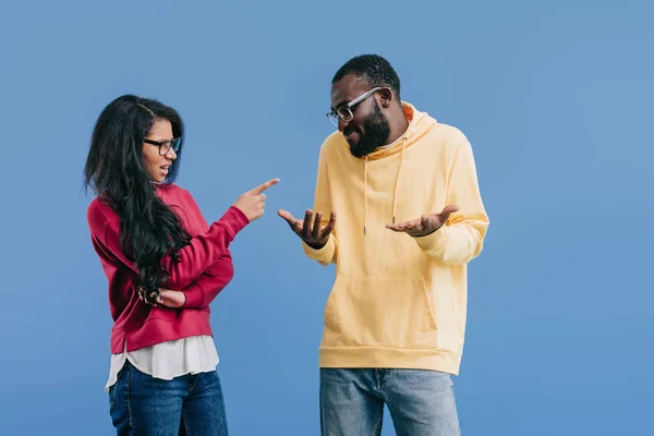 stock image angry african american woman pointing by finger at boyfriend doing shrug gesture isolated on blue background 