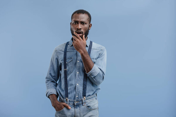 shocked african american man closing mouth by hand isolated on blue background 