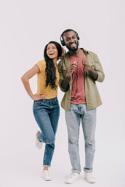 улыбающаяся африканская американская подружка подслушивает музыку бойфренда, изолированную на белом
