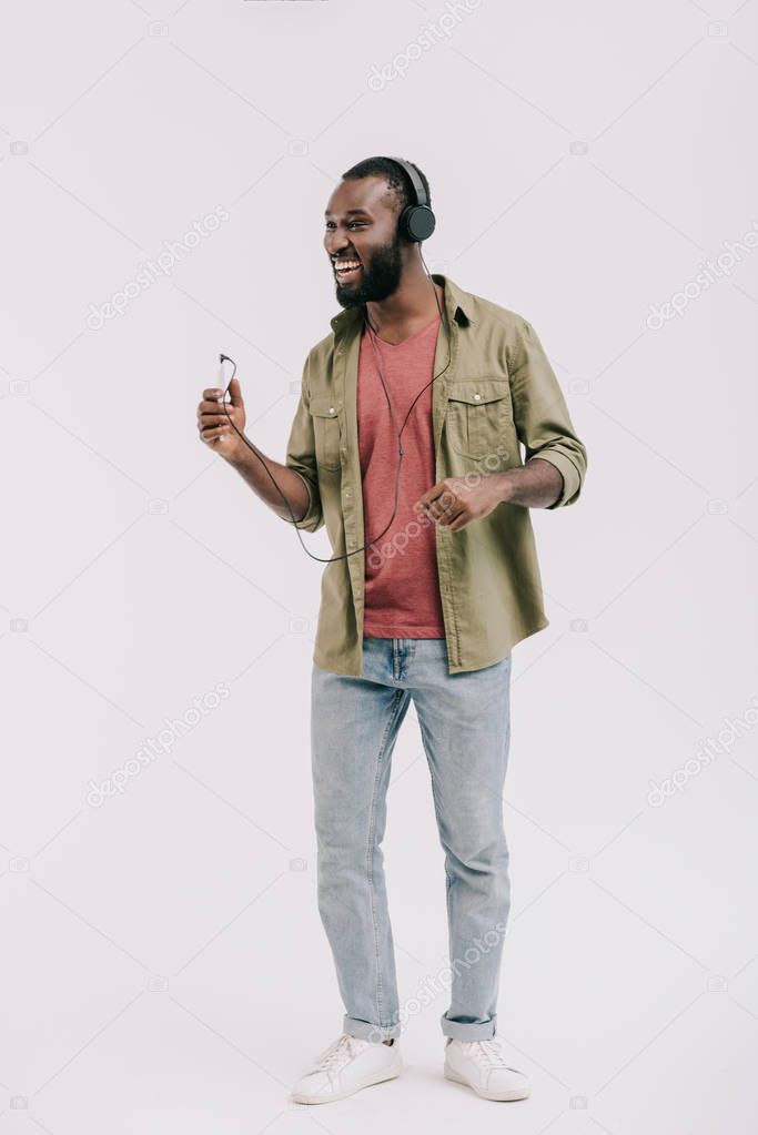 happy african american man listening music with smartphone and headphones isolated on white