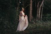 attraktive mystische Elfe im eleganten Blumenkleid, die im Wald spazieren geht