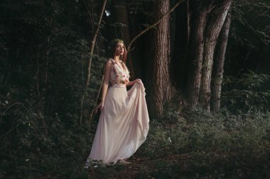 attractive mystic elf in elegant flower dress walking in woods clipart