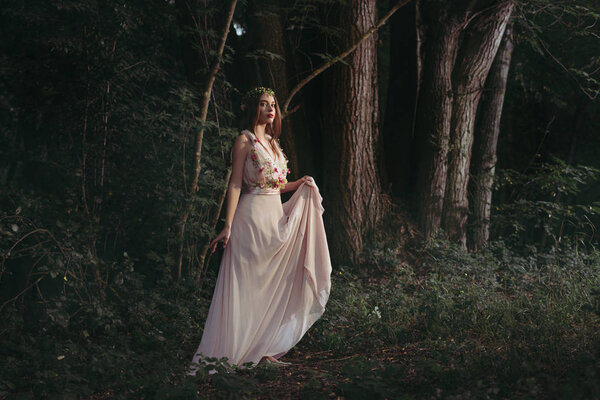 Attractive mystic elf in elegant flower dress walking in woods
