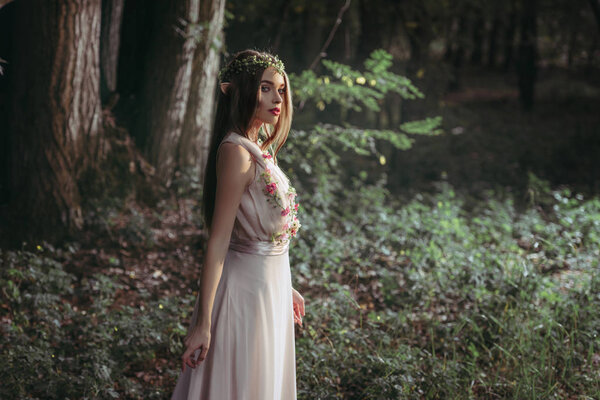 Beautiful mystic elf in elegant flower dress in woods
