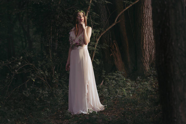 Elegant mystic elf in white dress with flowers in woods