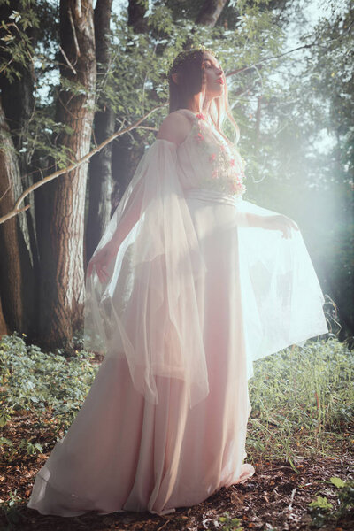attractive mystic girl in elegant dress posing in forest with sun flare