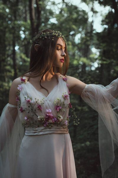mystic elf in floral wreath and dress with flowers in forest