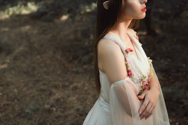 cropped view of elegant elf in dress with flowers standing with crossed arms