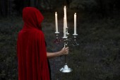 Mystic dívka v červený plášť, který drží svícen s hořící svíčky v temném lese