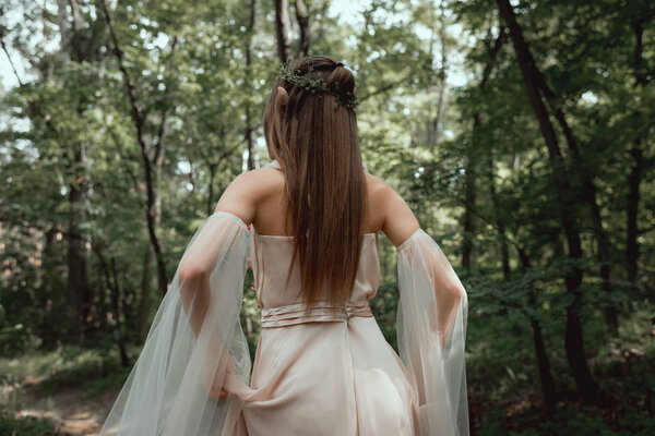 back view of mystic elf in elegant dress in forest