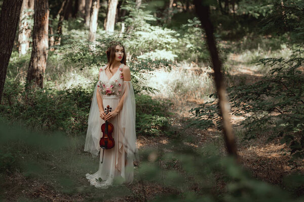 mystic elf in elegant dress holding violin in beautiful forest