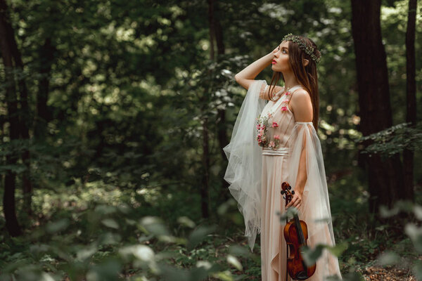 mystic elf character in flower dress holding violin in green forest