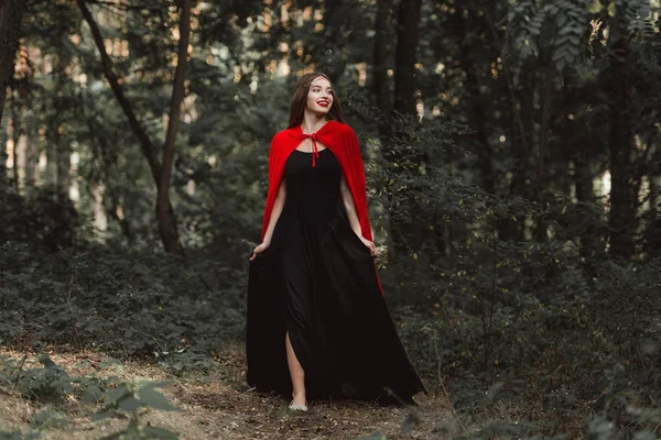 Hermosa Chica Mística Vestido Negro Capa Roja Caminando Bosque — Foto de stock gratuita