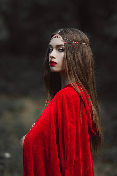 Attractive mystic girl in red cloak and wreath in forest