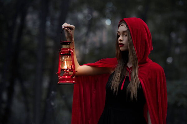 Mystic girl walking in dark forest with kerosene lamp