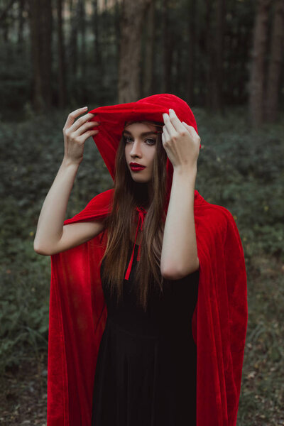 Attractive mystic girl in red cloak and hood in forest