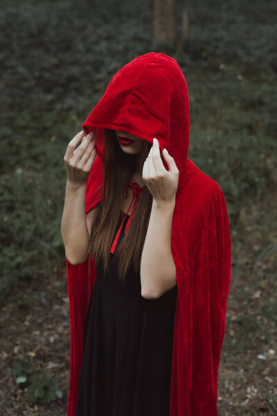 mystic woman in red cloak and hood in dark woods