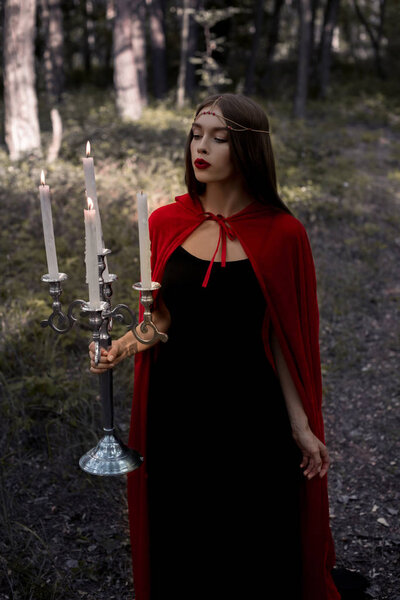 Beautiful magic girl holding candelabrum with flaming candles in woods
