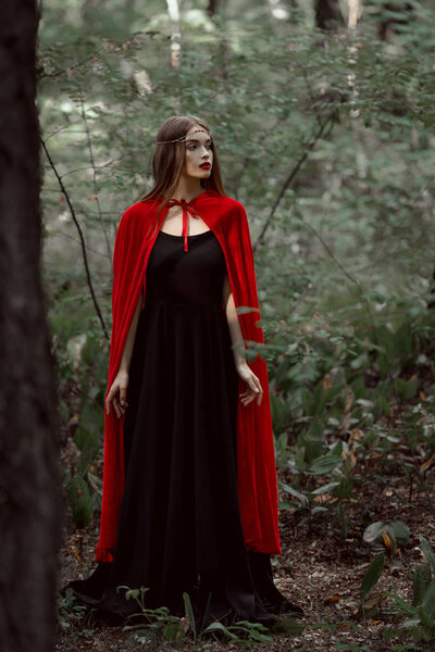 Beautiful mystic girl in red cloak in forest