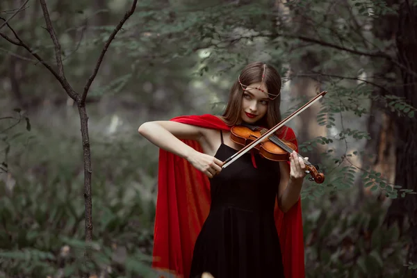 ヴァイオリンの森で遊んで赤いマントで魅力的な神秘的な女の子 — ストック写真
