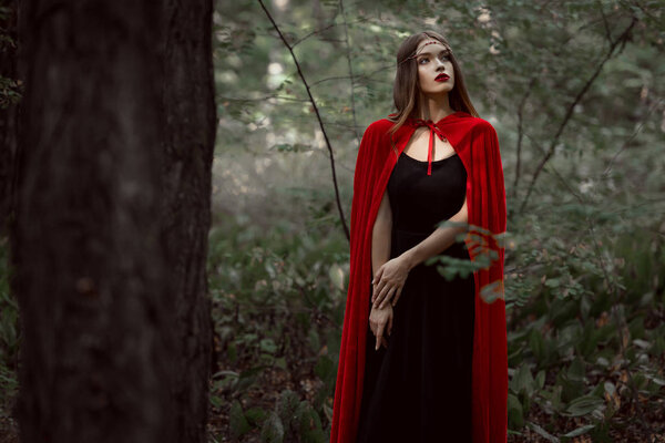 Attractive mystic girl in red cloak in forest