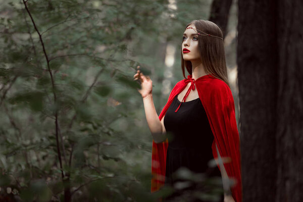 Mystic young woman in red cloak in forest