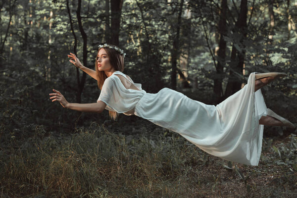 Elegant beautiful girl in white dress flying in forest