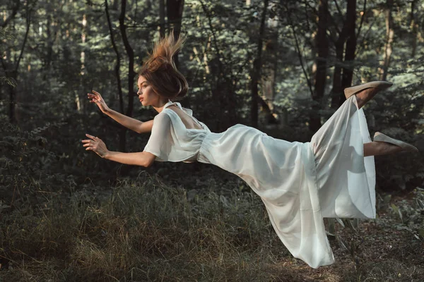 エレガントな若い入札フォレストを飛んでいる白いドレスの女性 — ストック写真