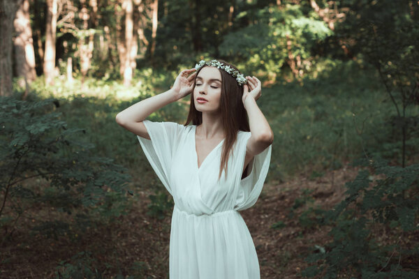 Tender girl with closed eyes posing in floral wreath in forest