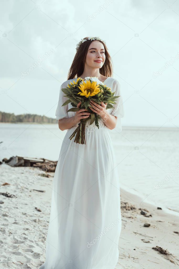 attractive girl in elegant dress holding bouquet with sunflowers on beach