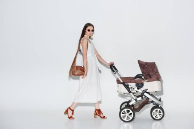 beyaz elbise ve bebek arabası ile yürüyüş ve gri kameraya bakarak güneş gözlüğü moda kadın 