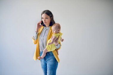 sevimli bebek kızı taşıyan ve yanında gri izole smartphone konuşmak güzel şık Anne