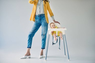 şık Anne Grey yüksek sandalyede oturan bebek kız yakın duran kırpılmış atış