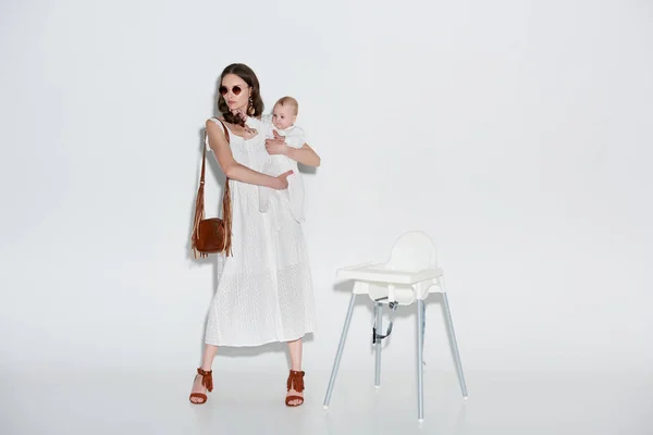 Stylish Woman Carrying Adorable Baby Girl Standing High Chair Grey — Stock Photo, Image