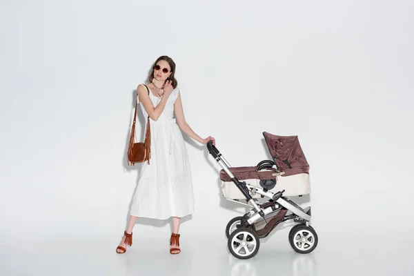 Stijlvolle Vrouw Witte Jurk Zonnebril Poseren Met Kinderwagen Grijs — Stockfoto