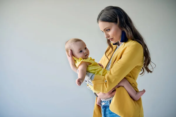 美丽时尚的母亲抱着可爱的婴儿女儿灰色孤立的侧面视图 — 图库照片