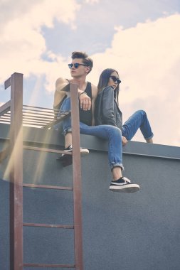 şık çok ırklı çift güneş gözlüğü güneş ışığı ile çatıda oturan